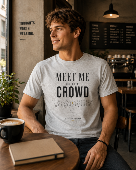 Man wearing a white Meet Me in the Crowd graphic T-shirt in a warm café