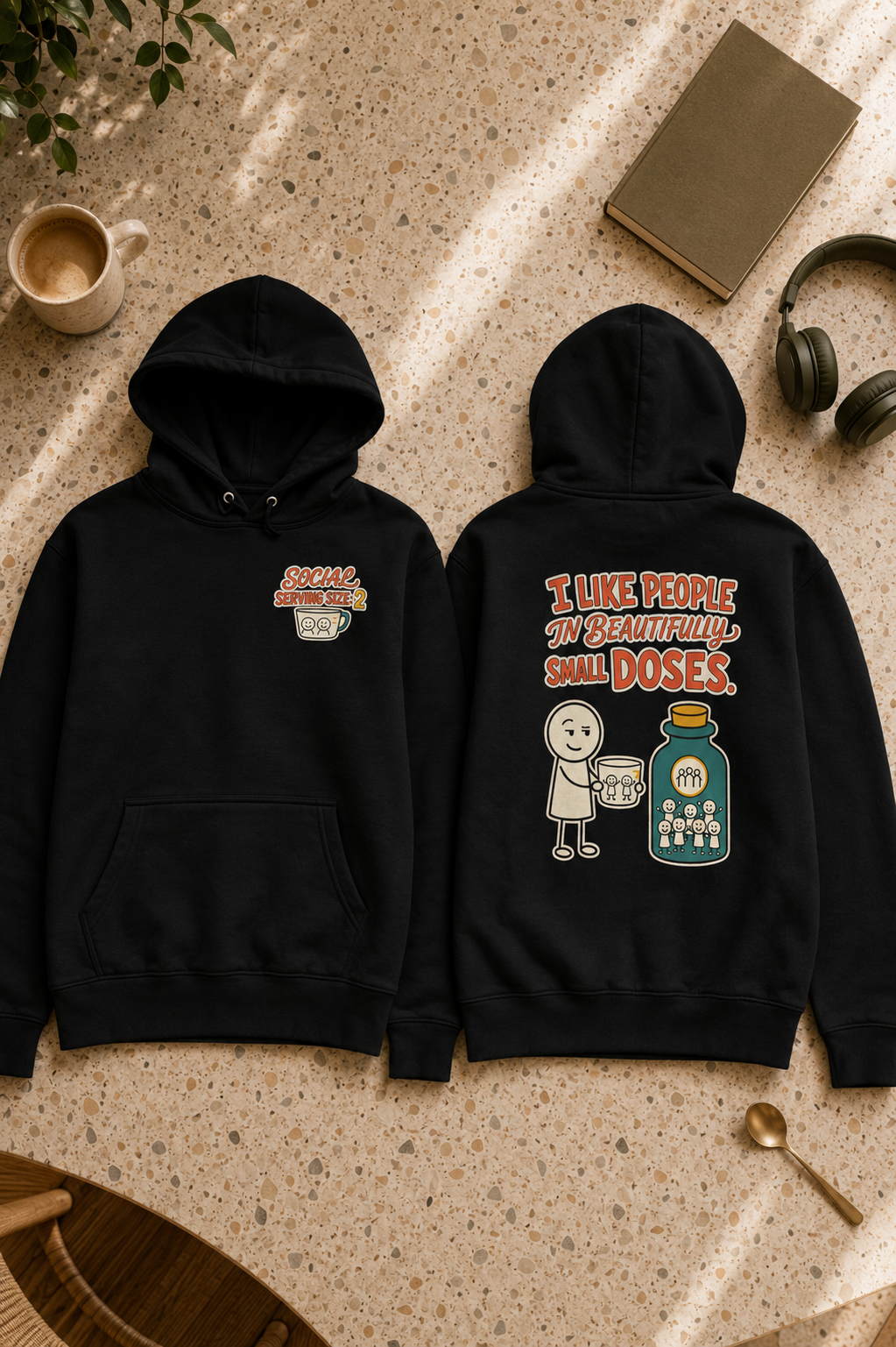 Two black hoodies laid flat on a speckled beige surface, showing the front and back designs. The front has a small chest graphic with a coffee cup and the words 'SUGAR CRUSH'.