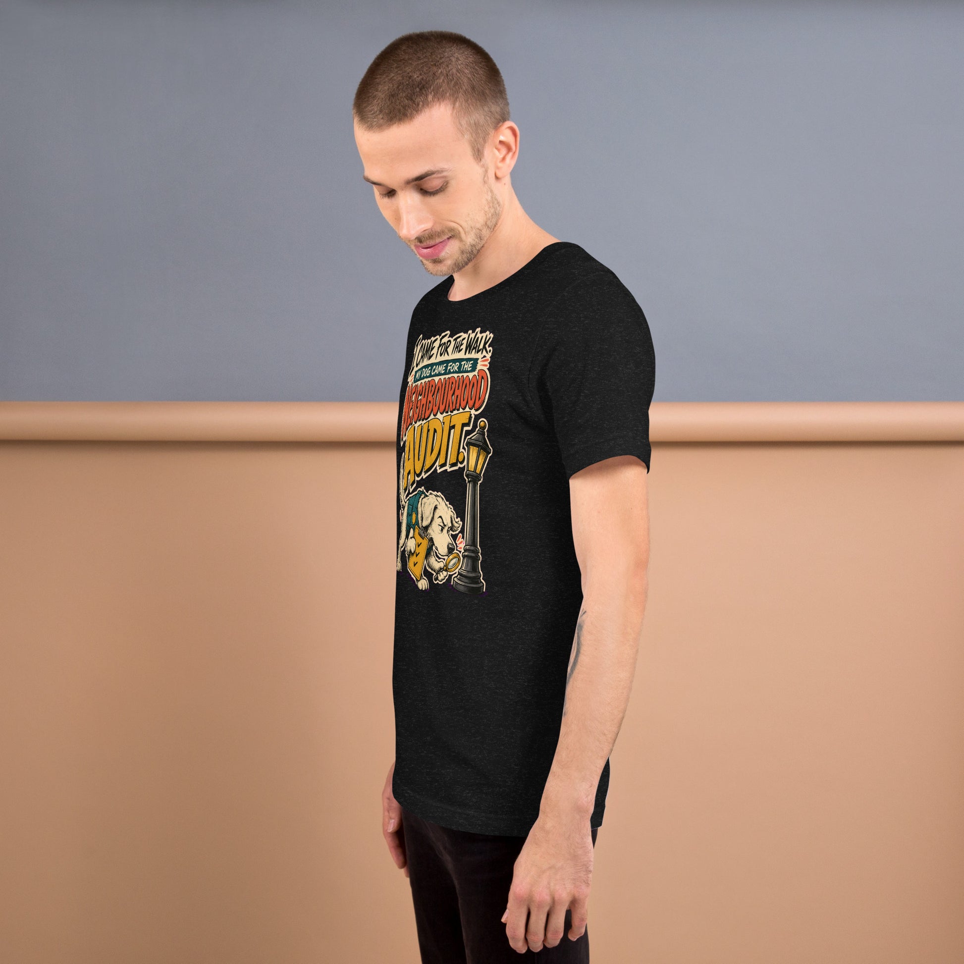 A man wearing a black graphic t-shirt with a vintage-style 'The Addams Family' poster print, standing against a two-tone gray and beige studio background.